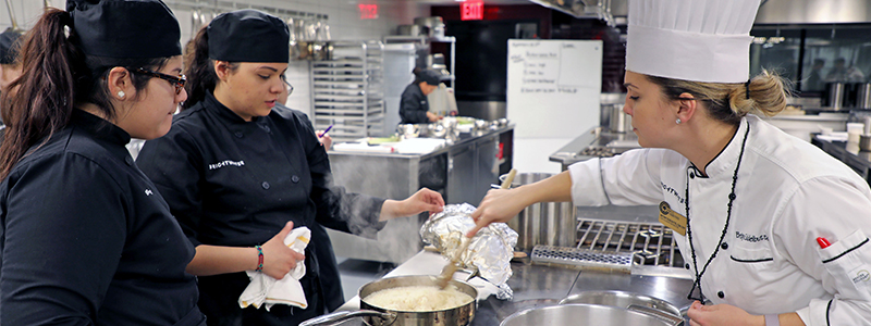 Female chef stiring a pot and teaching two female culinary students