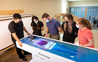 Table Showing the Anatomy of a Human Body With Students Standing Around It. 