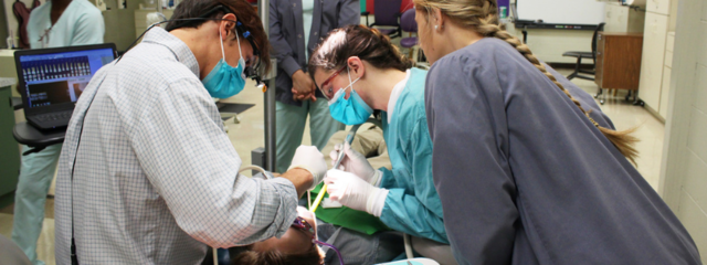 Man and Two Women Hover Over Patient in Chair